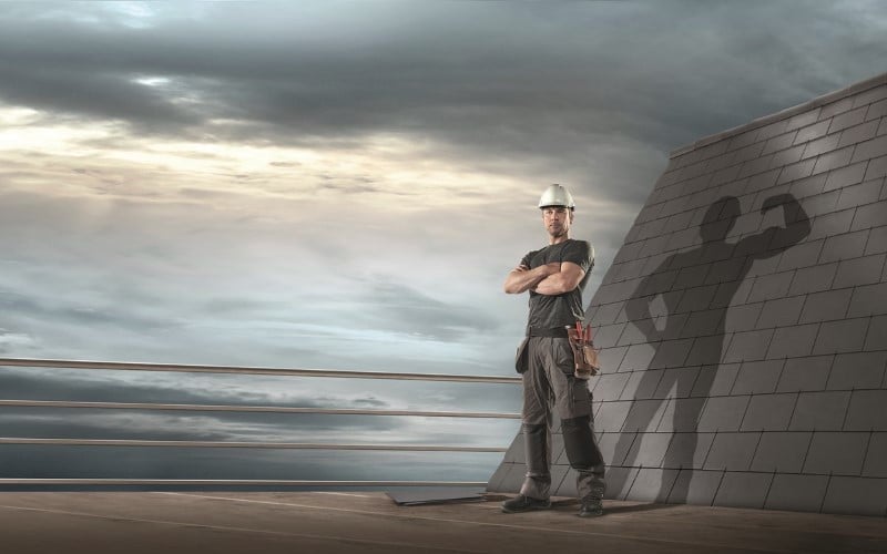 grey dressed Cedral worker standing on a grey roof top on the right grey weatherboard slates