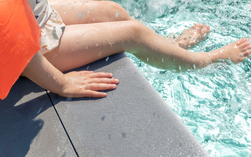 woman wearing orange blouse legs on a grey facade feet are put in swimming pool