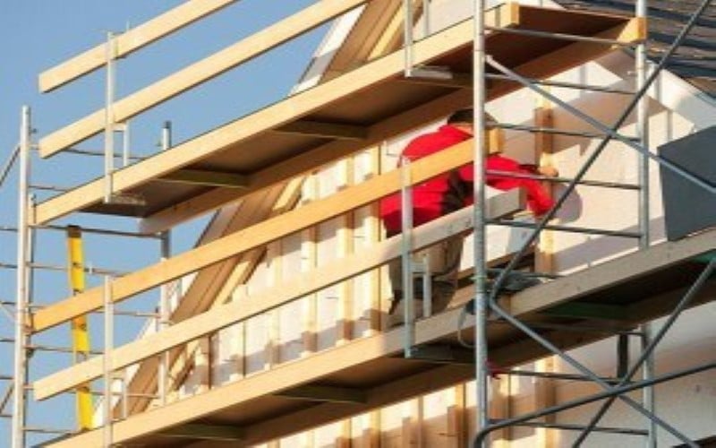 red man installing sand colour weatherboards on a house on the left light blue skye