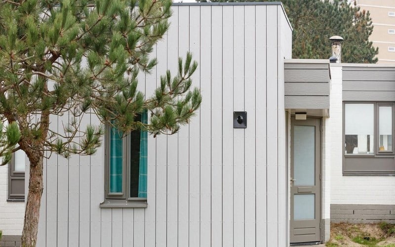 white weatherboards house on the left green tree on the right light brown doors