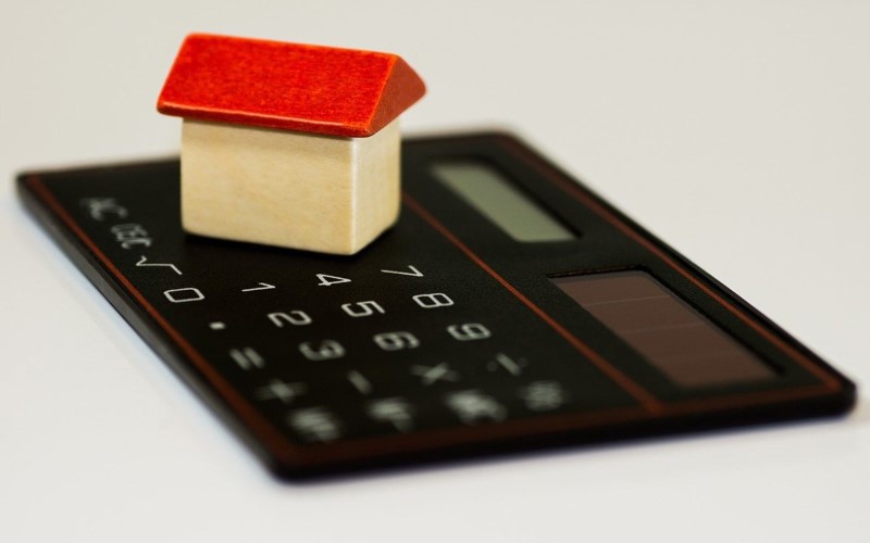 black calculator below it white background on top of it tiny wooden house with red roof