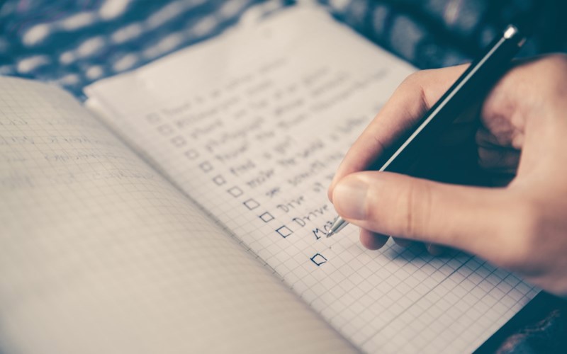 white notebook with blue pen writings and a hand holding black pen on a right