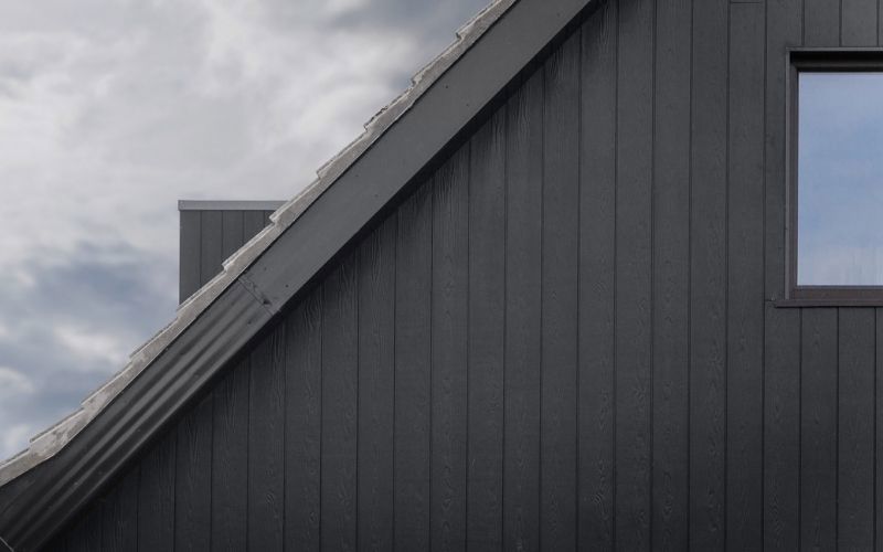dark grey siding on a house exterior wall on the left white and blue sky