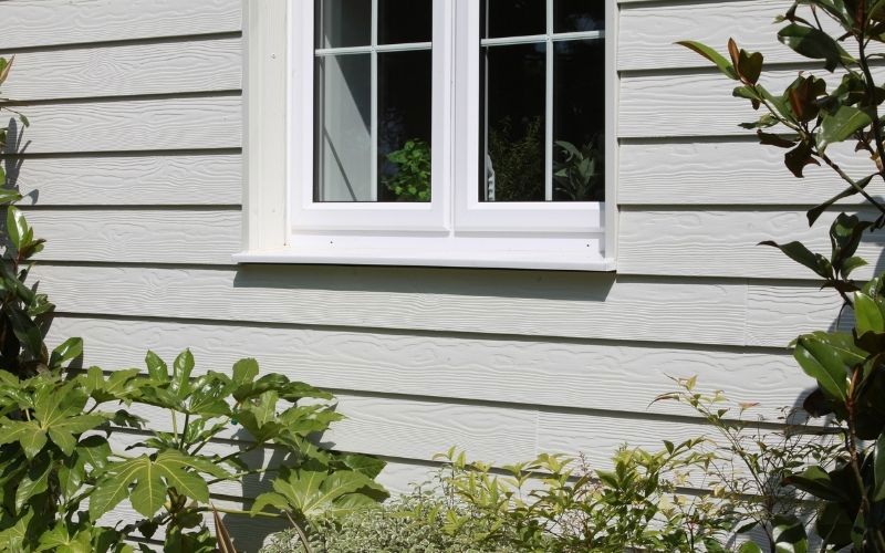 white Cedral weatherboard siding of a wall white frame window in the middle and green grass below