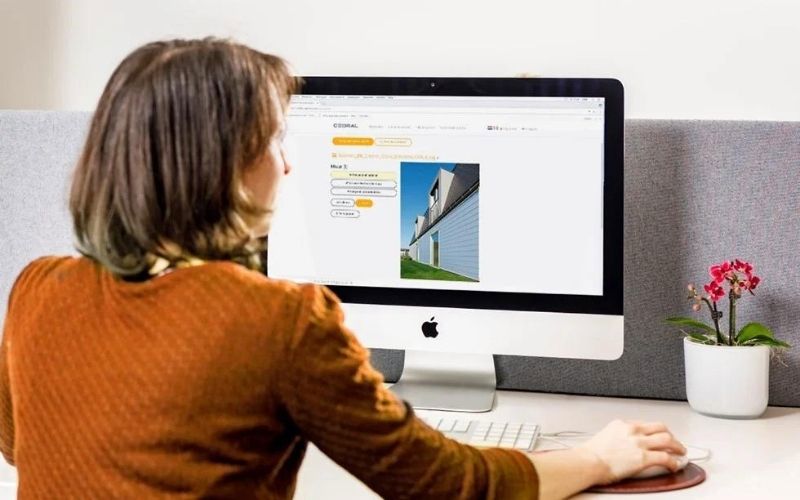 woman with orange shirt is sitting behind white iMac facing computer