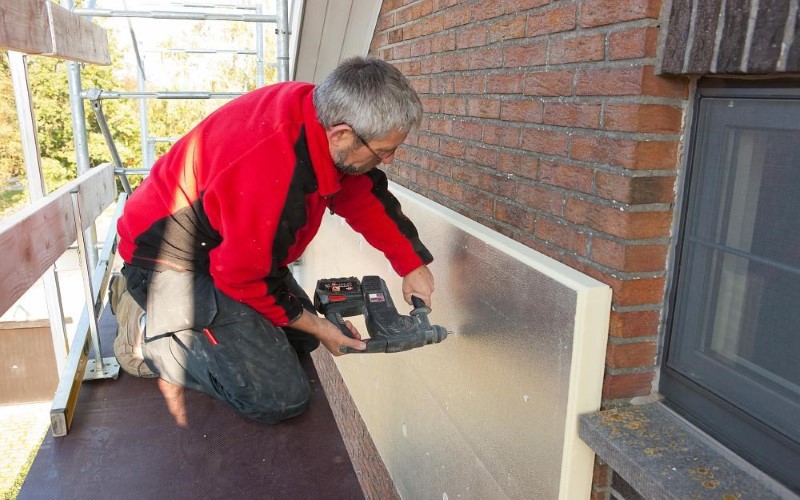 Installer dressed red insulating the outside of a house